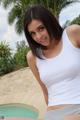 A woman in a white tank top posing by a pool.