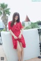 A woman in a red dress sitting on a white wall.