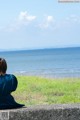 A woman in a blue dress sitting on a wall looking out at the ocean.