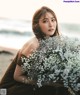 A woman sitting on a beach holding a bunch of flowers.