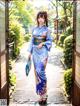 A woman in a blue kimono standing in front of a gate.