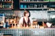 A woman behind a bar with bottles of alcohol behind her.